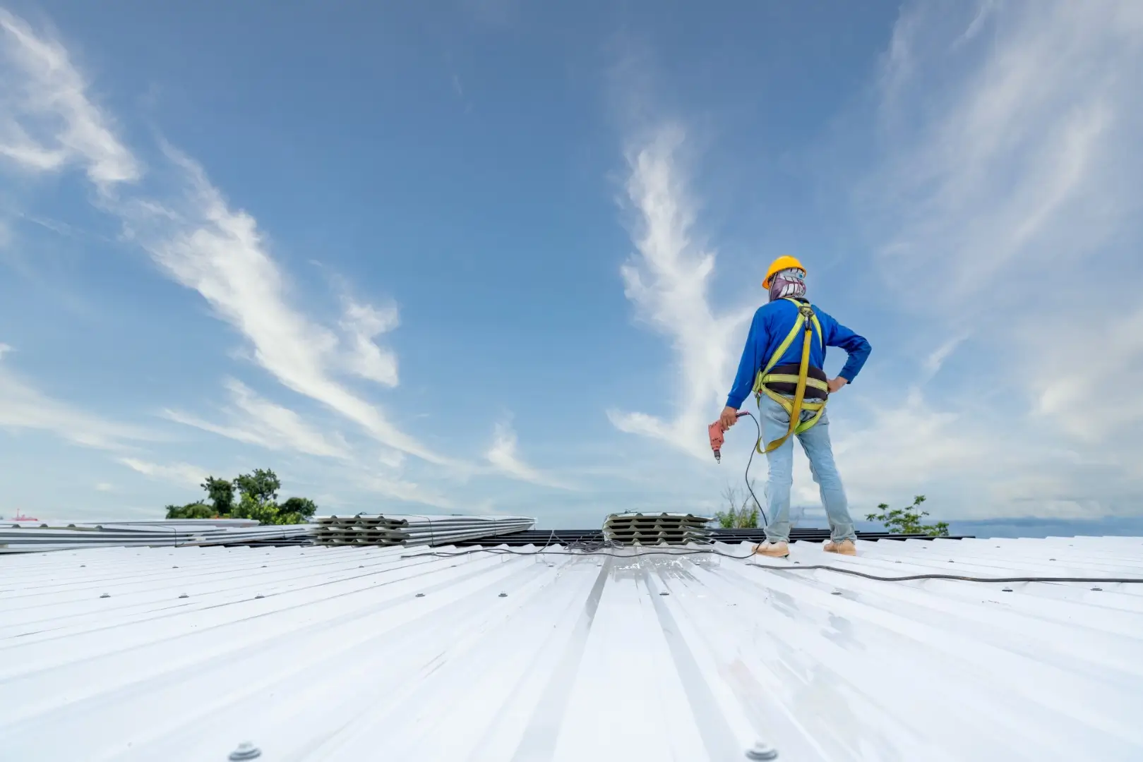A Roofer using electric drill nail gun installing PU foam roof sheet at under construction.