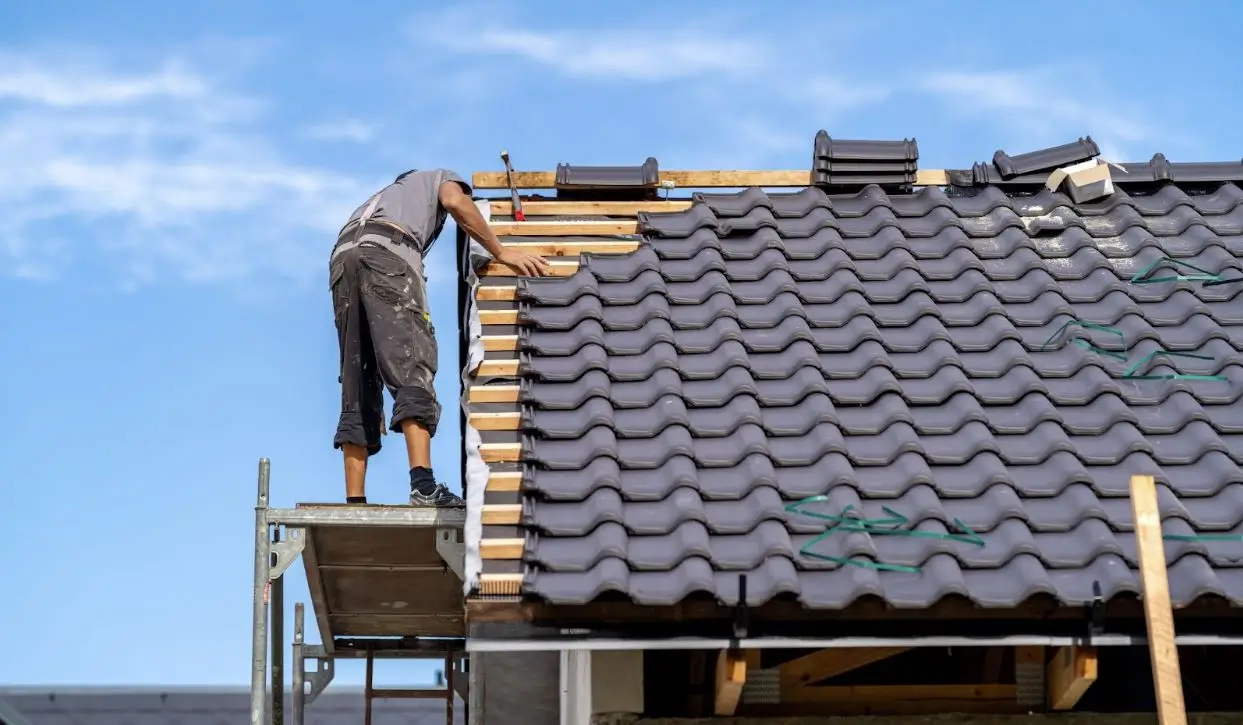 A male builder installing gray ceramic tiles on the roof of a family home, carefully constructing a durable and elegant roof covering.