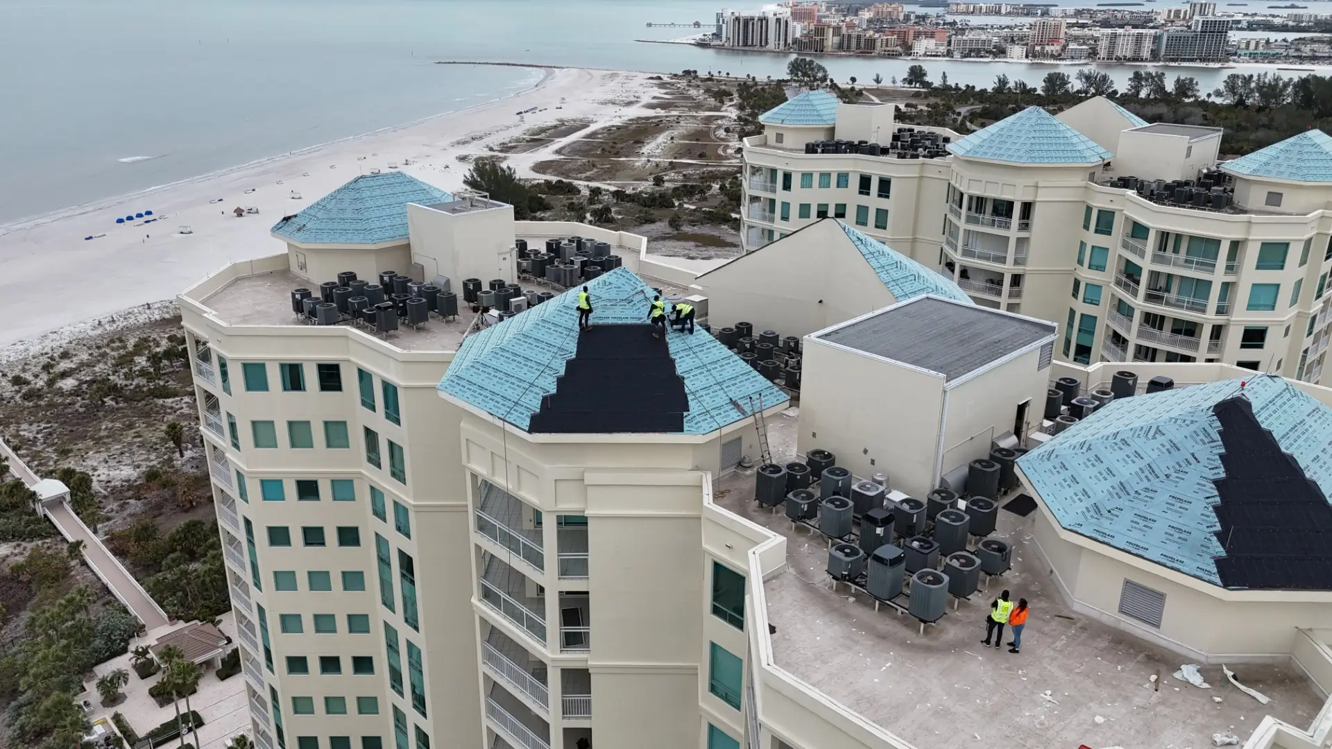 Aerial view of high rise apartments with teal colored roofs in the process of being installed.
