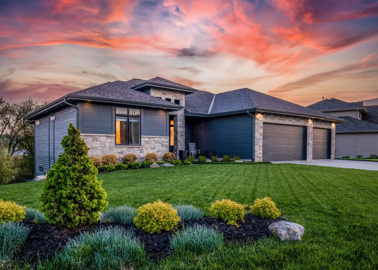 Luxury home during twilight golden hour with pink and purple sky and lush landscaping.