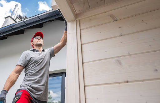 A worker inspects the exterior of a house before installing new gutters.