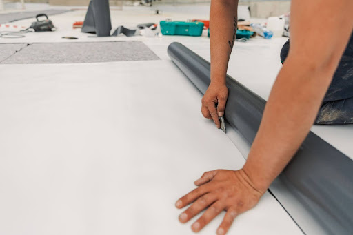 A worker carefully cuts a TPO roofing membrane sheet to ensure precise alignment during installation.