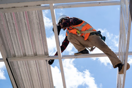 A low-angle shot of a roofer in a protective suit installing roofing materials on a high structure.