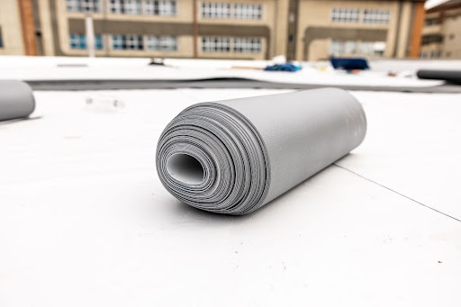 A tightly rolled sheet of TPO roofing membrane on a flat surface, ready for installation on a commercial roof.