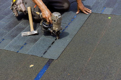 Overhead shot of a roofer using a nail gun to install bitumen roof shingles.