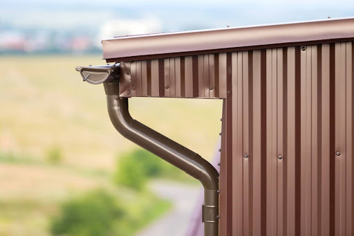 Close-up of a brown cottage house corner with metal siding, roof, and gutter system.