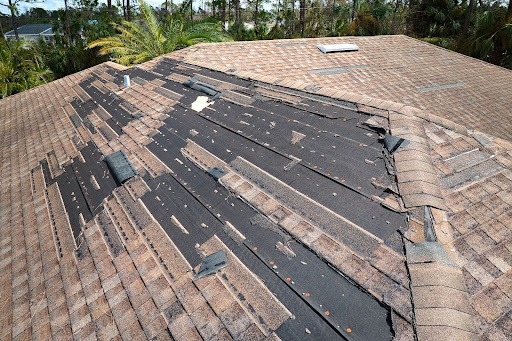 House roof with missing asphalt roof shingles due to wind damage.