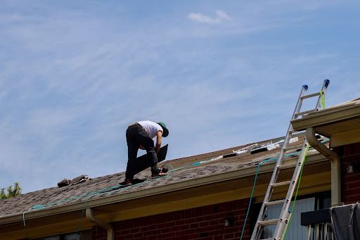 Roofer replacing gray roof shingles with a ladder resting on the side.