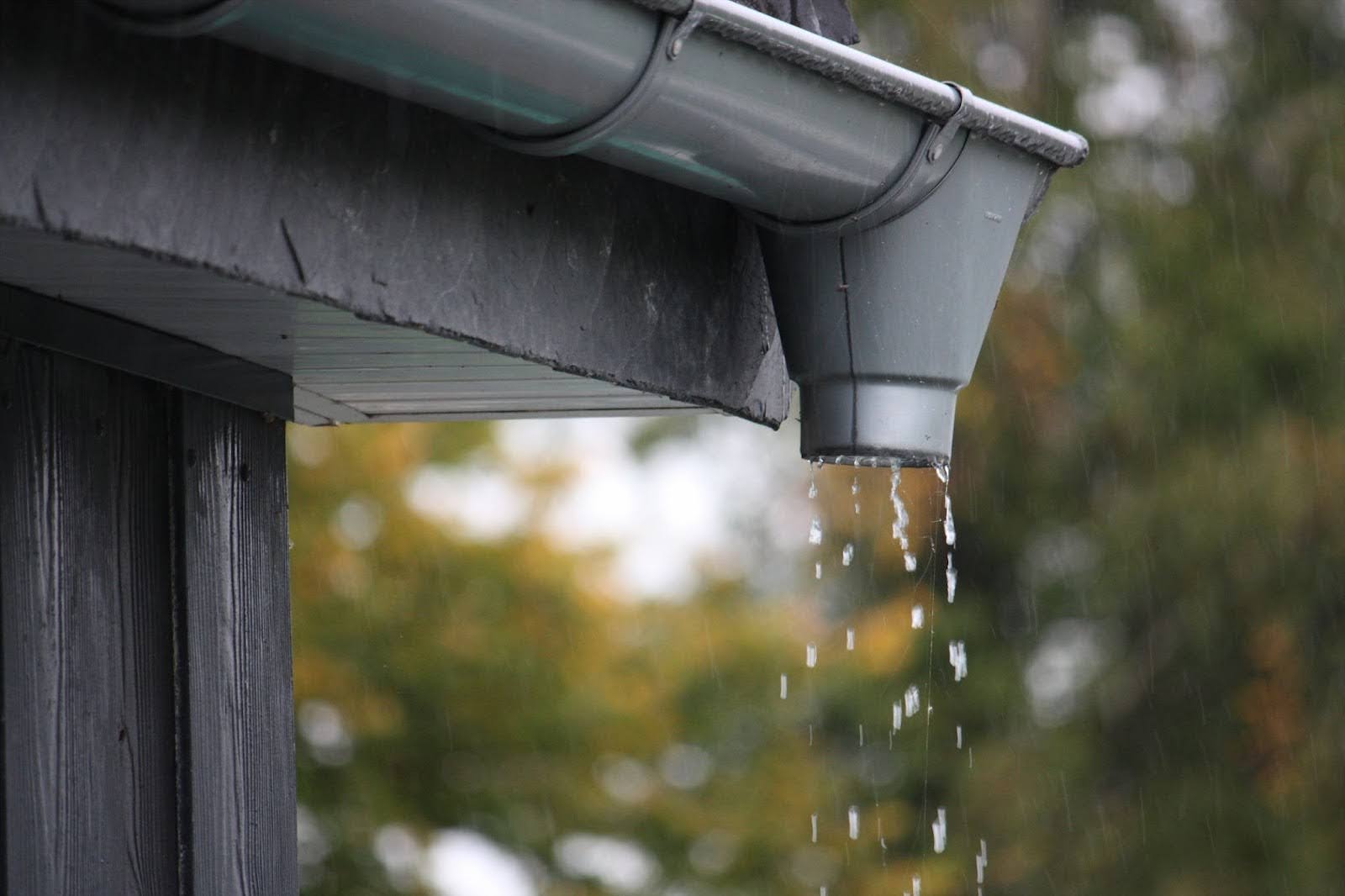Closeup of water droplets falling from the roof rain gutter during rainfall.
