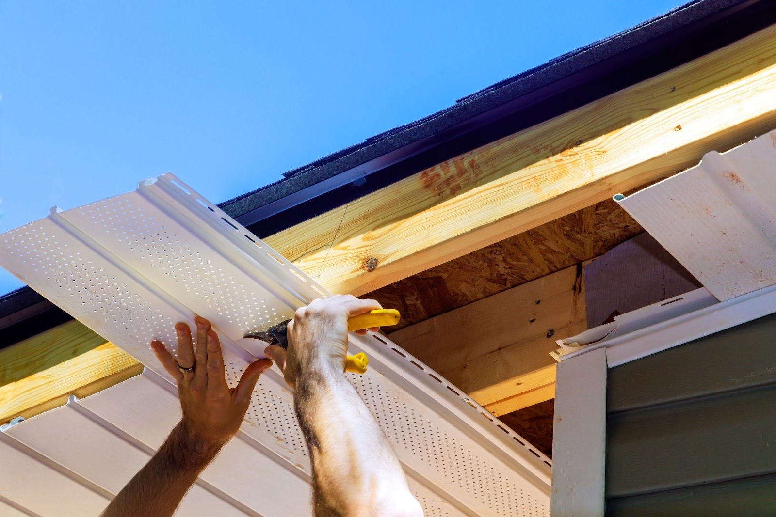 A contractor is installing vinyl soffit panels on the facade ceiling of a modern house.