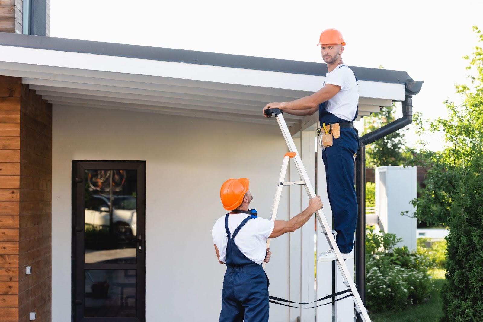 Two workers prepare to install gutters on the side of a house.