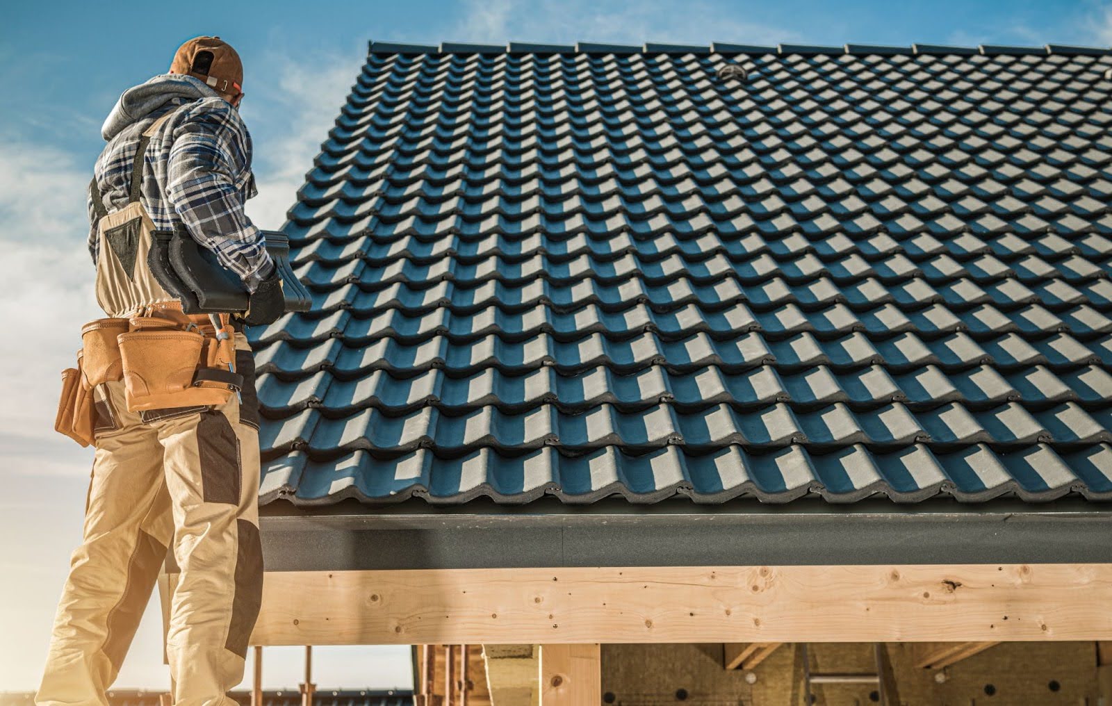 A roofing worker installs gray tiles on top of a home.