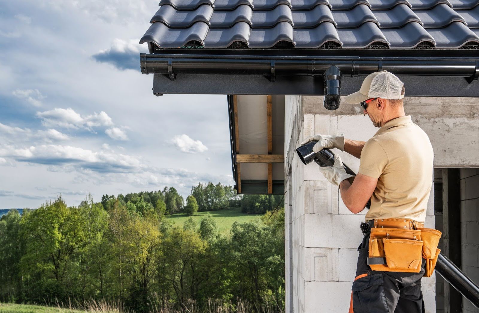 A man installs black gutters along a home’s sloped roofing edge.